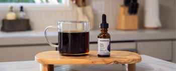 A bottle of Medterra Daily Relief CBD oil next to a cup of coffee on a wooden surface.