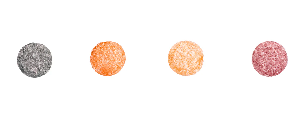 Top-down view of four round sugar-coated CBD gummy candies in gray, orange, peach, and pink on a white background