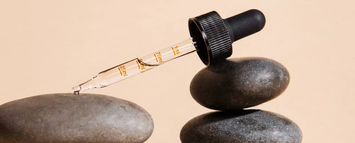 A dropper bottle of CBD and CBG oil tincture resting on stacked stones