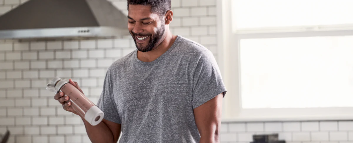 A man smiling while holding a water bottle in a kitchen setting.
