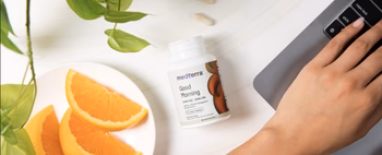 A hand reaching for a bottle of Medterra Good Morning supplement next to orange slices.