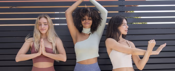 Three women practicing meditation in stylish activewear against a slatted backdrop.