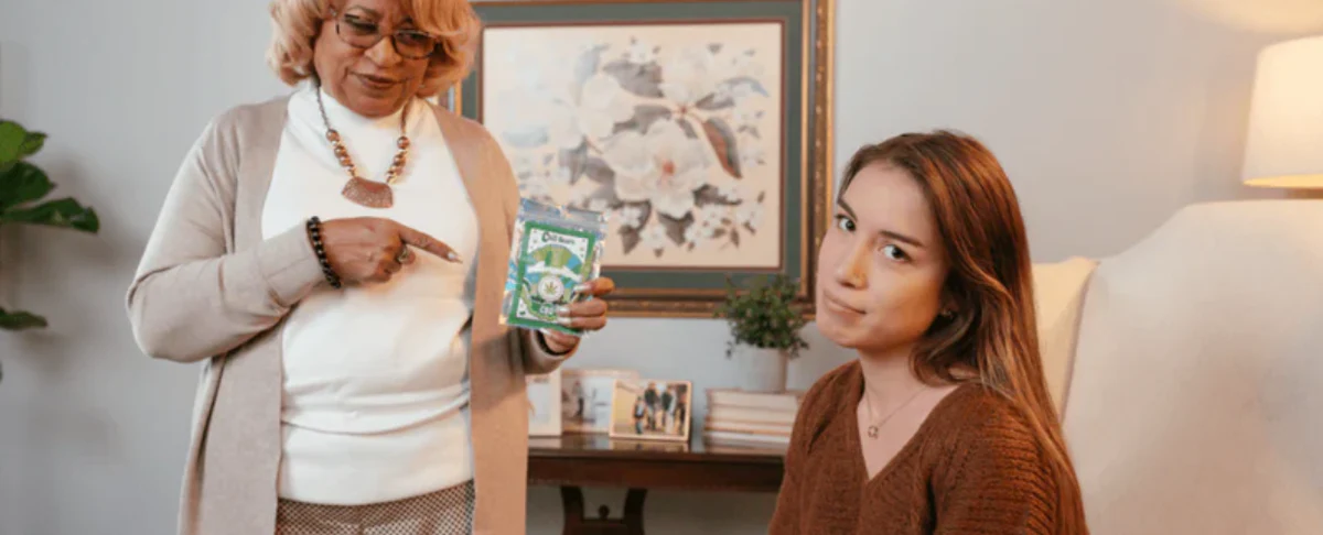 An older woman points to a CBD product while speaking to a younger woman, who looks thoughtful.
