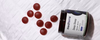 A jar of Medterra Deep Sleep CBD gummies with red gummies scattered around it.