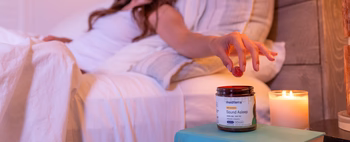 A woman reaching for a jar of Sound Asleep CBD gummies on a bedside table.