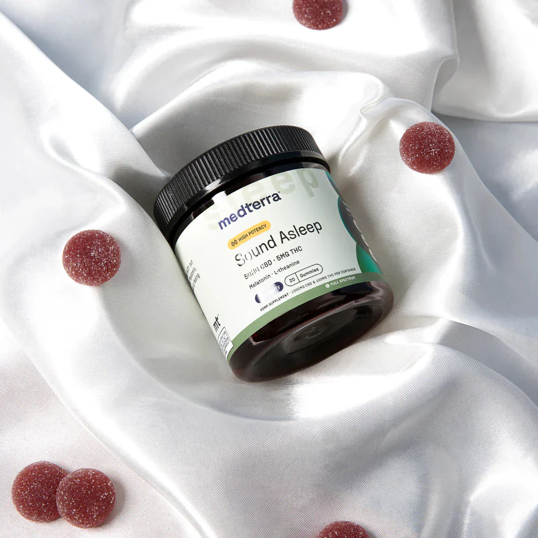 medterra Sound Asleep HIGH POTENCY Melatonin L-theanine Gummies jar on white satin, red sugar-coated gummies nearby