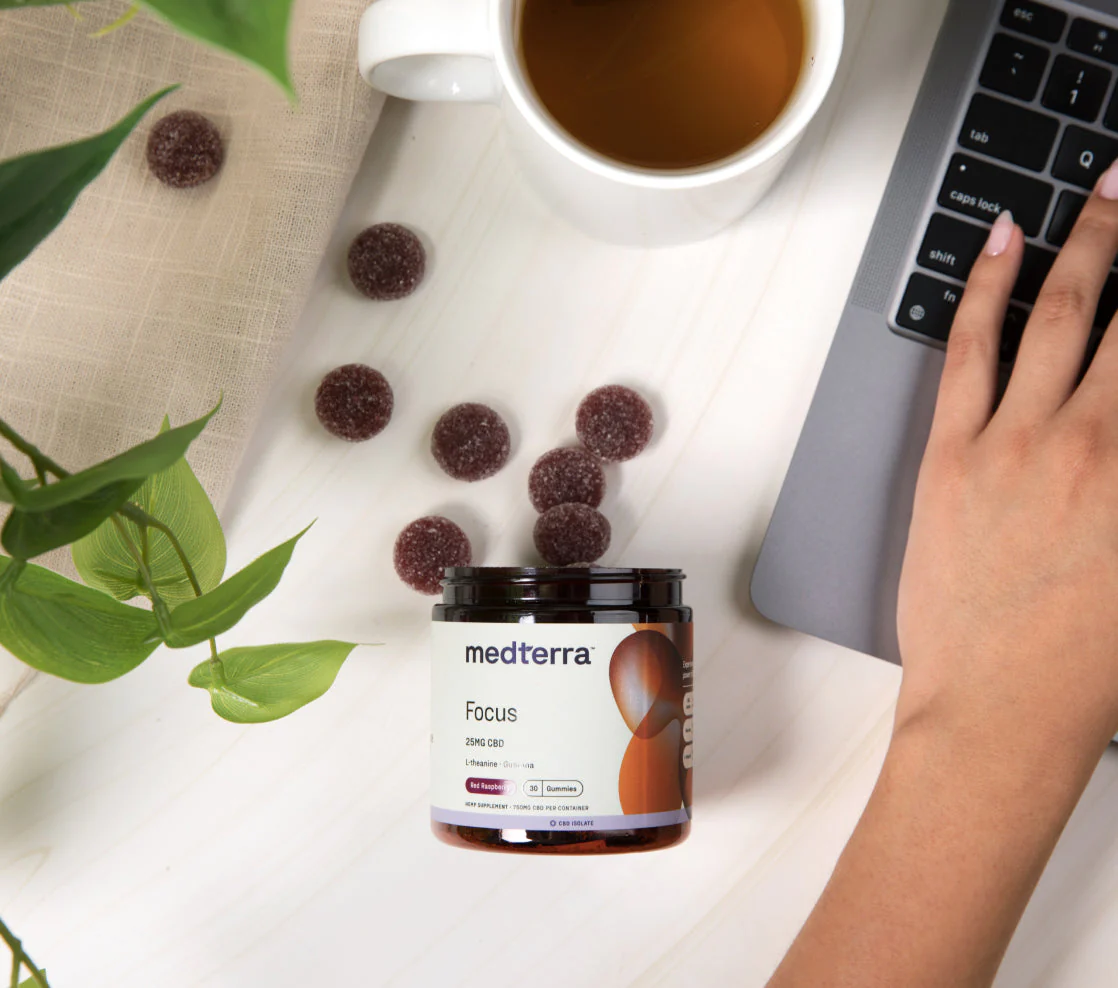 medterra Focus; 25MG CBD L-theanine Red Raspberry Gummies; scattered gummies, cup, laptop keys: tab caps lock shift fn esc