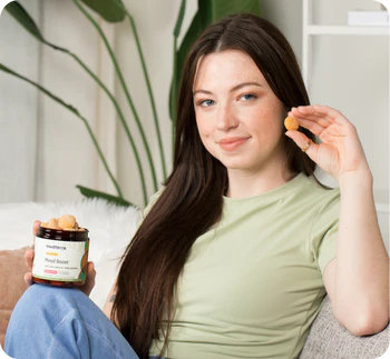 Young woman holding a jar labeled medterra Mood Boost and holding a single yellow CBD gummy.
