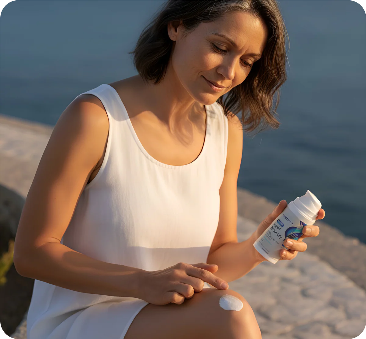 Woman in white sleeveless top applying a white recovery cream to her knee from a pump bottle