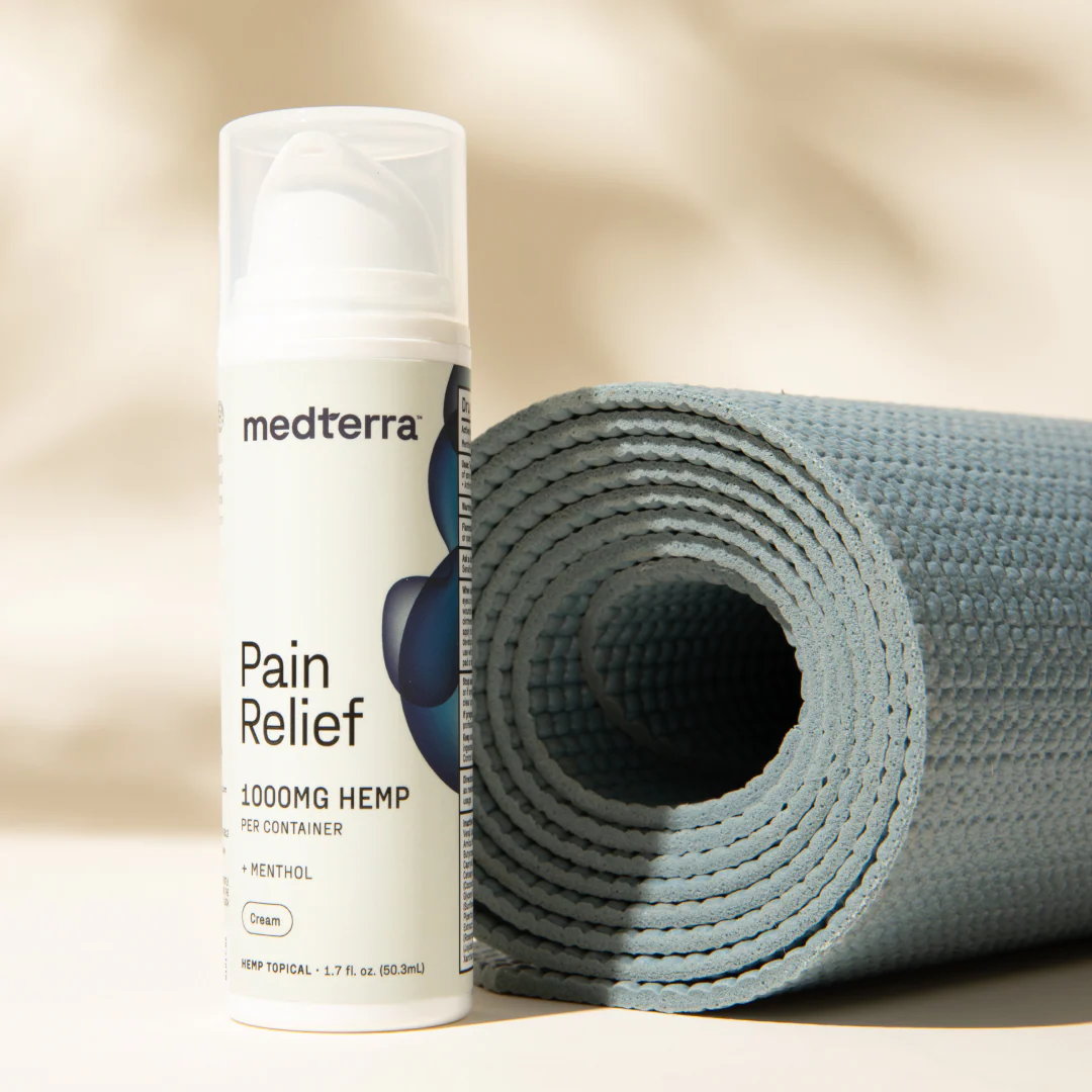 Front view of Pain Relief Cream bottle with pump-top, 1000mg hemp, 1.7 fl oz and menthol label beside a rolled blue yoga mat