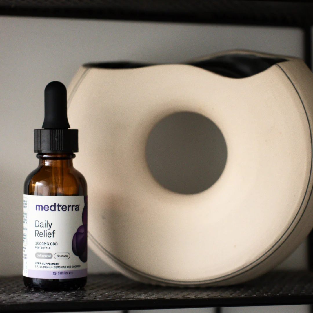 Front view of Daily Relief CBD Isolate 1000 mg oil bottle with dropper lid and label against blurred shelf and ceramic vase