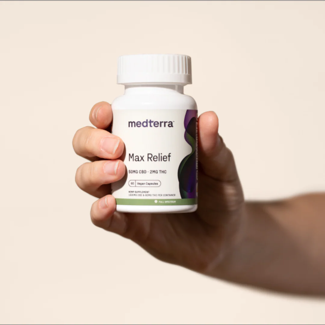 Front view of Medterra Max Relief capsules bottle held in hand showing 50mg CBD, 2mg THC against soft beige background