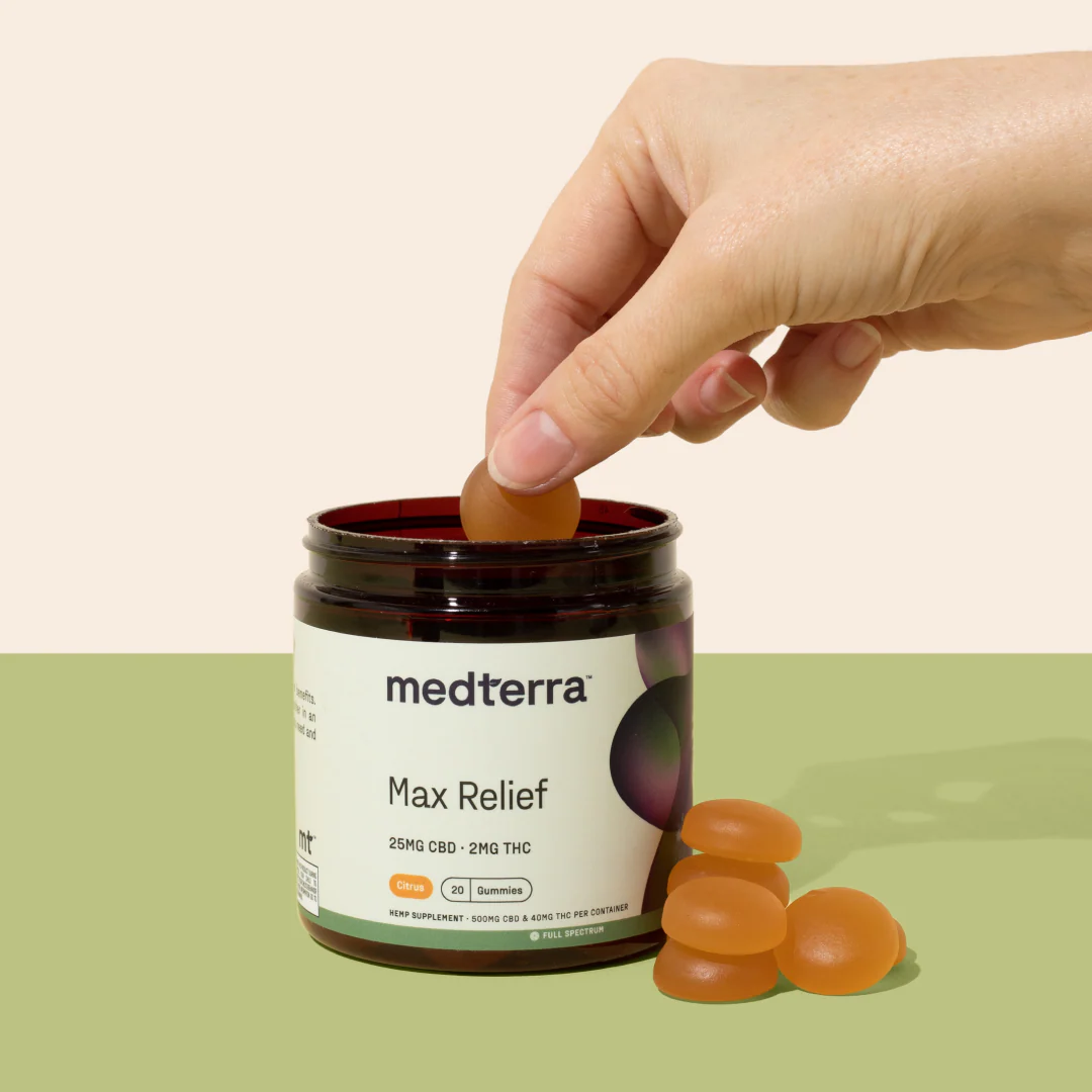 Close-up of Max Relief Full Spectrum CBD Gummies jar with a hand lifting one gummy, label showing 25 mg CBD · 2 mg THC, pastel background
