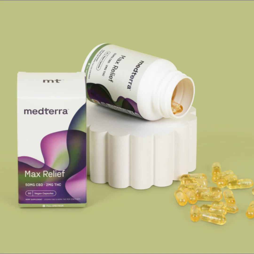 Angled view of Medterra Max Relief capsules with box and tipped bottle spilling yellow capsules on a scalloped pedestal