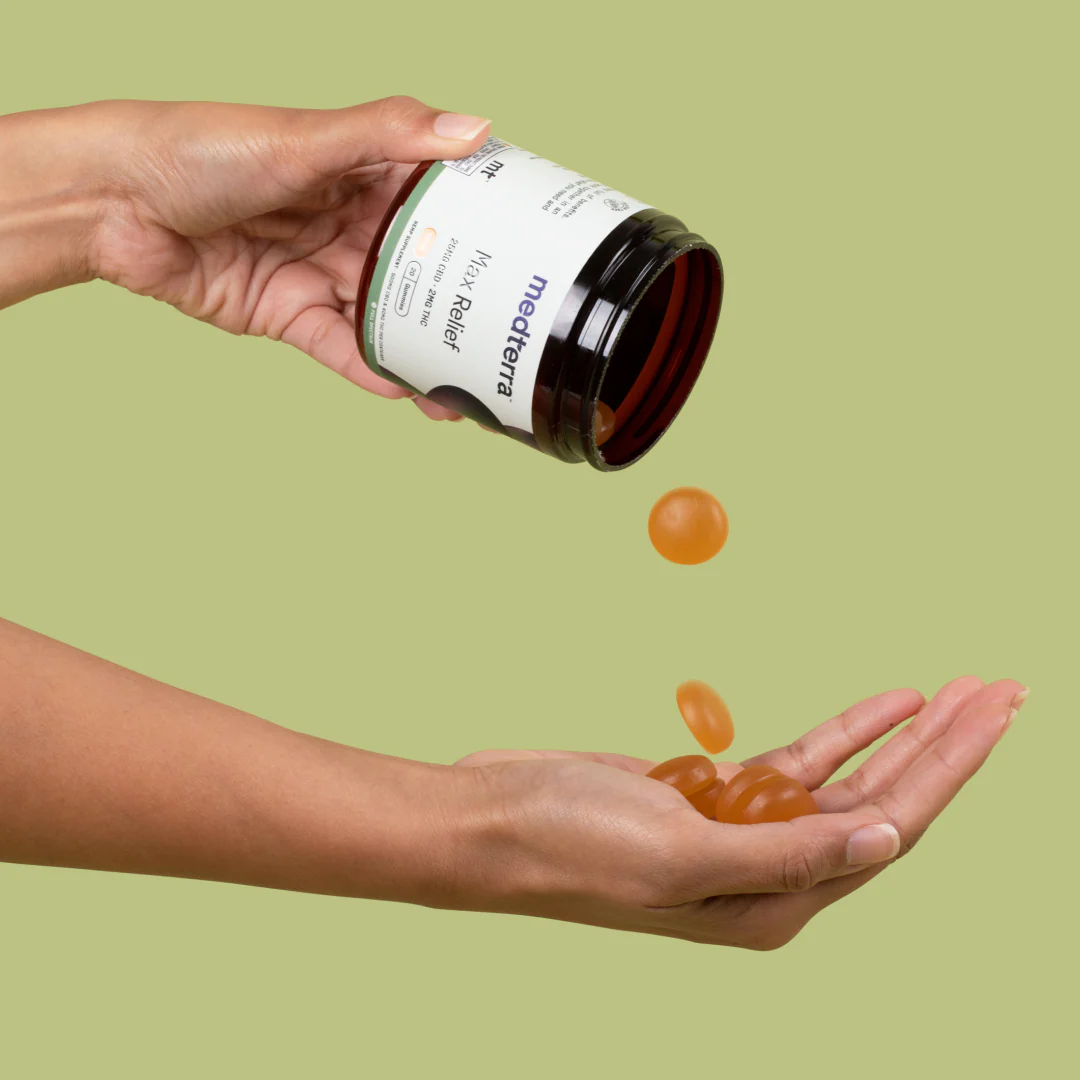 Angled view of Max Relief CBD Gummies jar pouring amber gummies into a cupped hand on a light green background