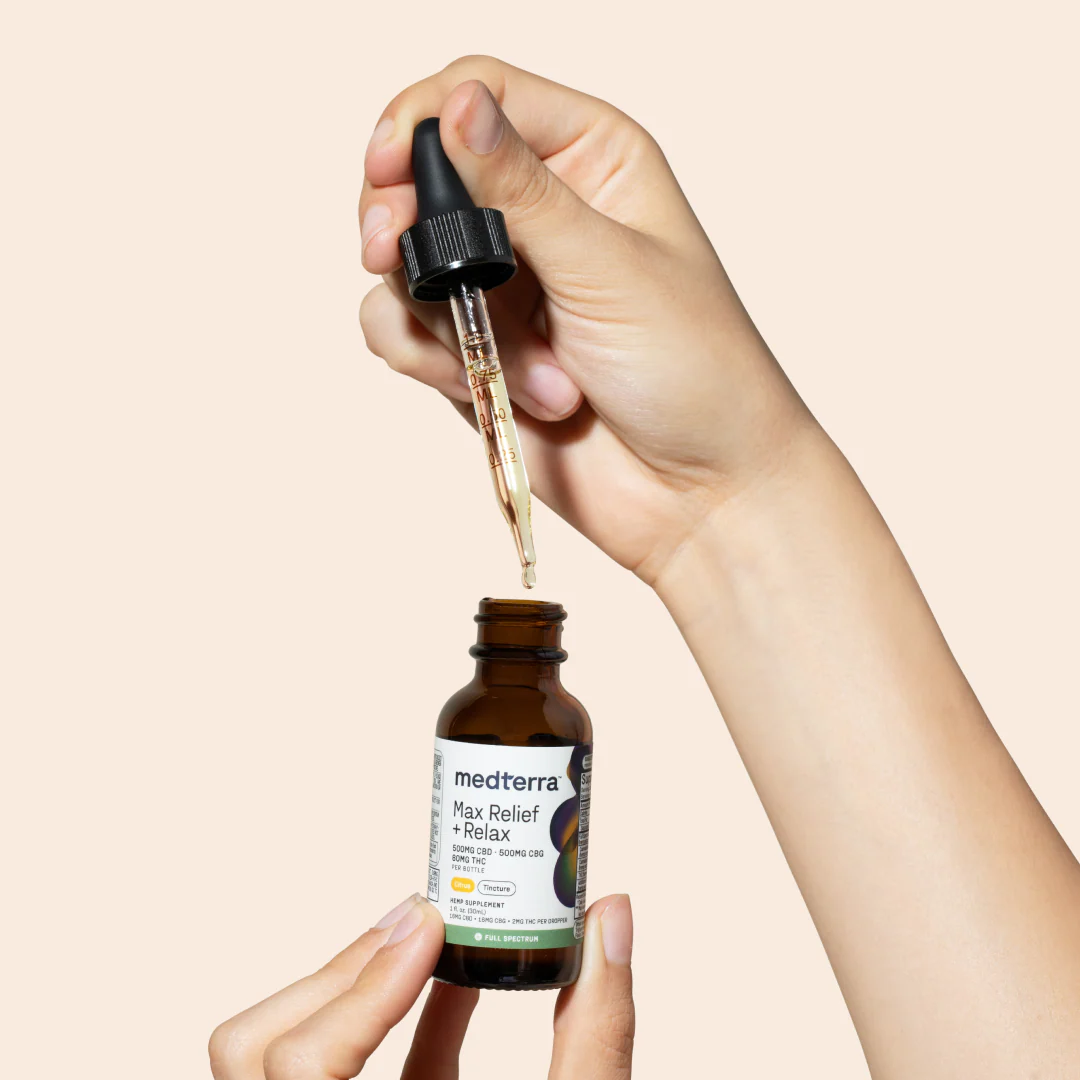 Close-up of Medterra Max Relief + Relax full-spectrum CBD oil bottle with dropper and oil droplet on peach background
