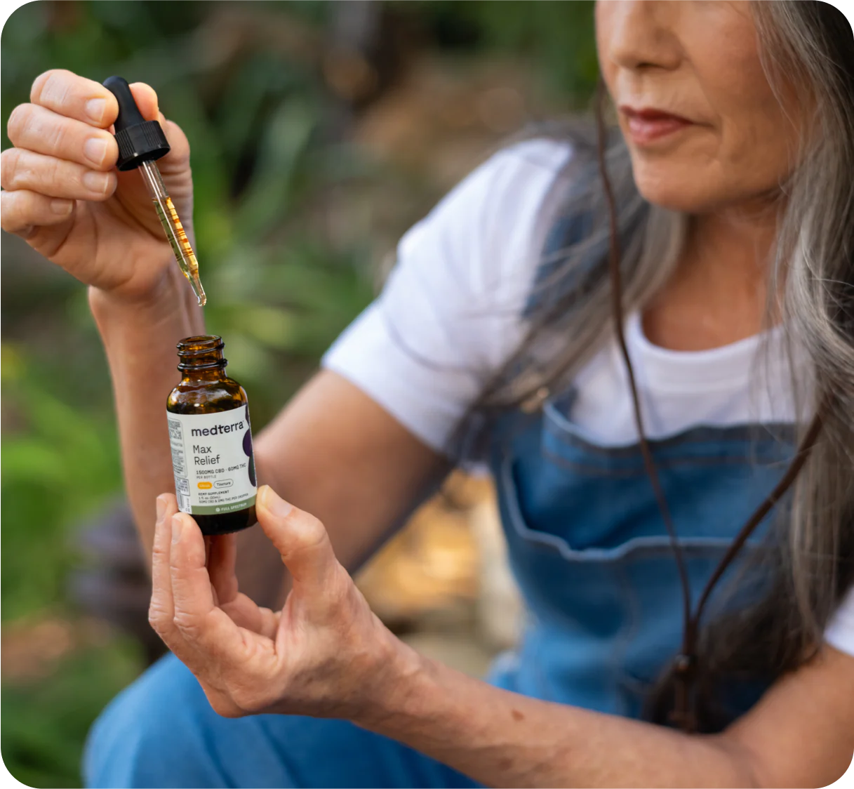 Woman using a dropper to dispense Medterra Max Relief CBD oil from an amber bottle outdoors