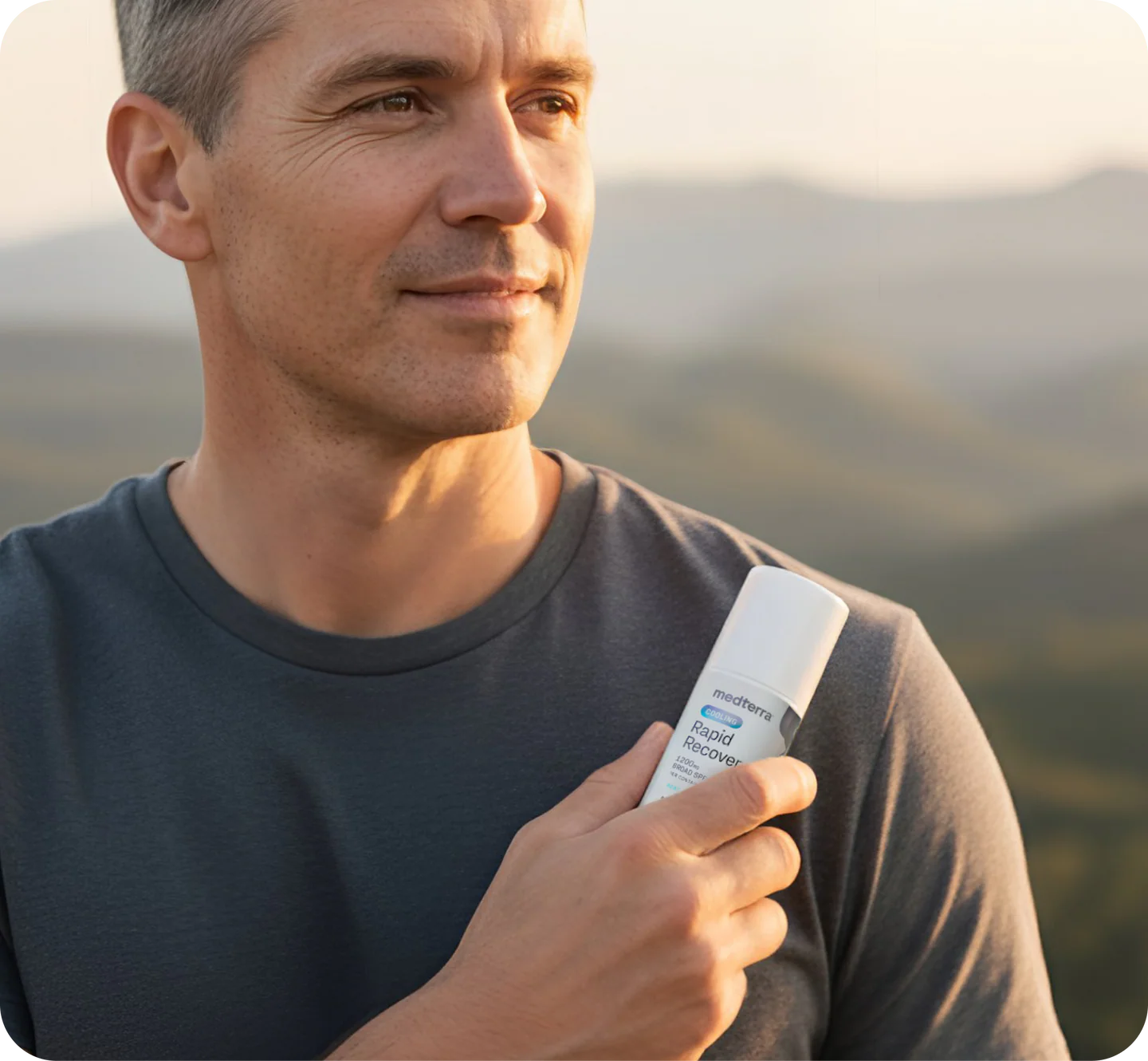 Man holding roll-on product labeled medterra Rapid Recover against distant hills at sunset, gazing right.