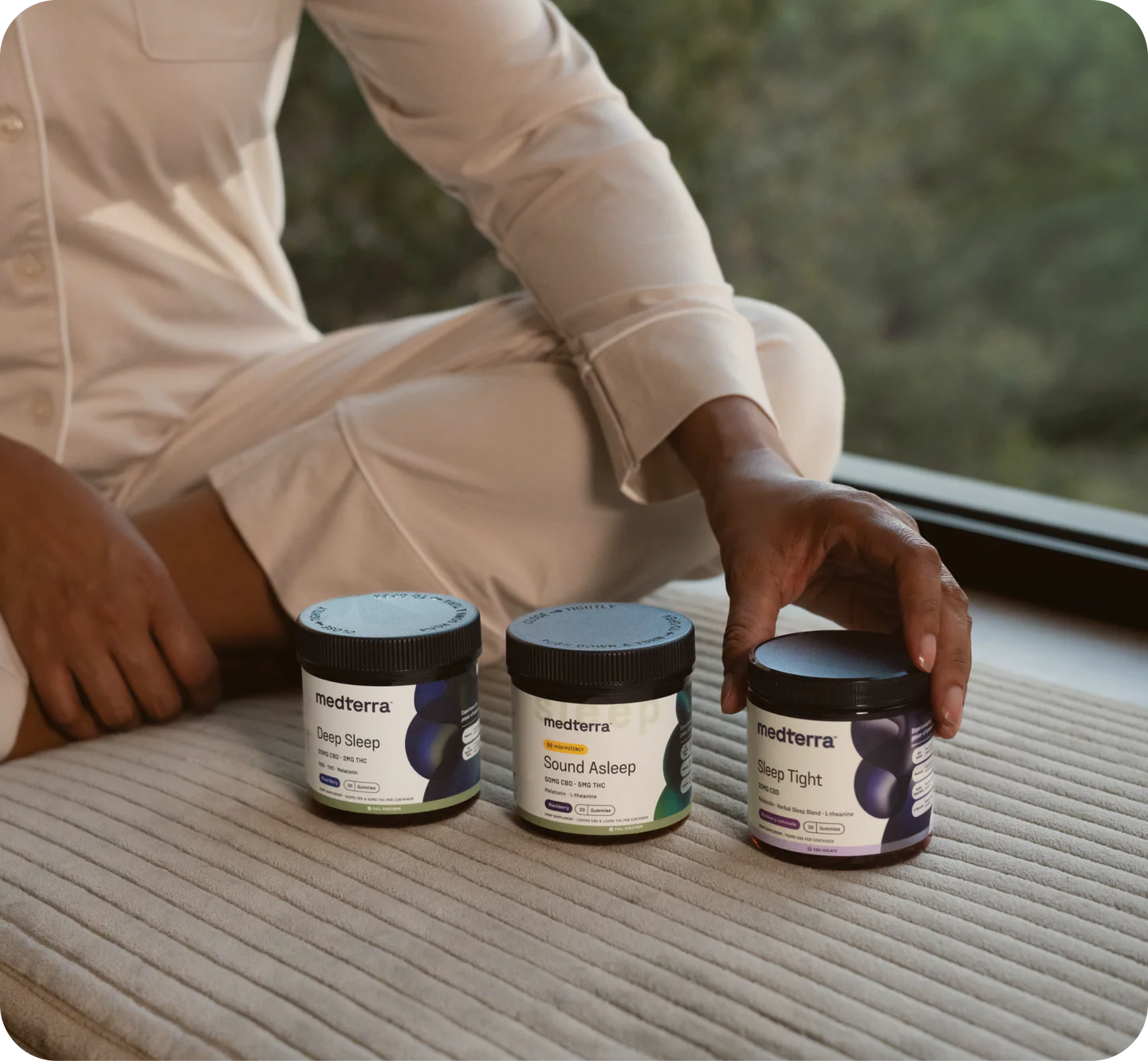 Three medterra jars labeled Deep Sleep, Sound Asleep, and Sleep Tight on a bed; a hand reaches for the right jar.