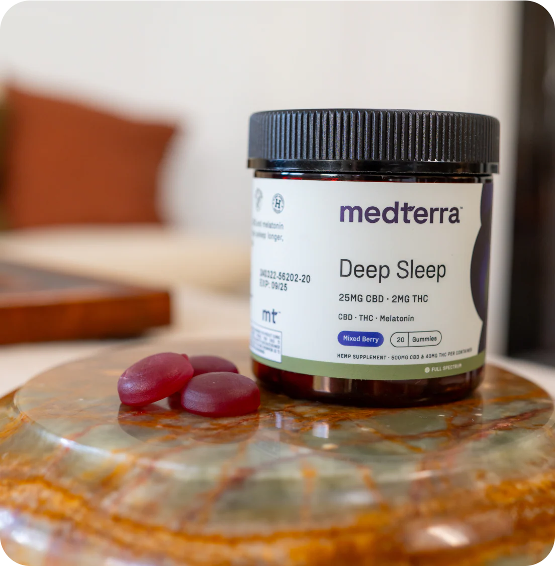 Front view of Medterra Deep Sleep jar showing label 25 mg CBD, 2 mg THC and three mixed berry gummies on a stone coaster