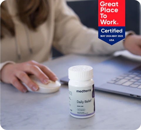 Medterra Daily Relief bottle on office desk with employee using mouse and laptop, Great Place To Work Certified badge visible