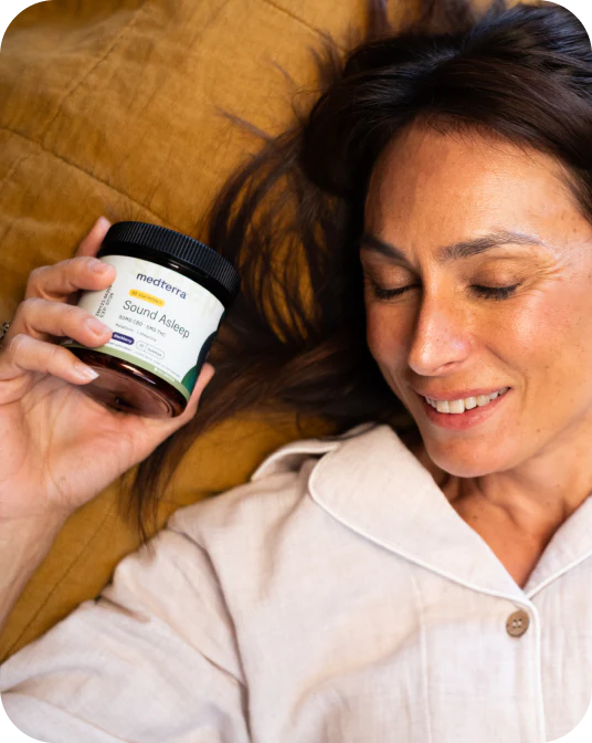Woman reclining on a pillow in pajamas, eyes closed, holding a jar labeled medterra Sound Asleep.