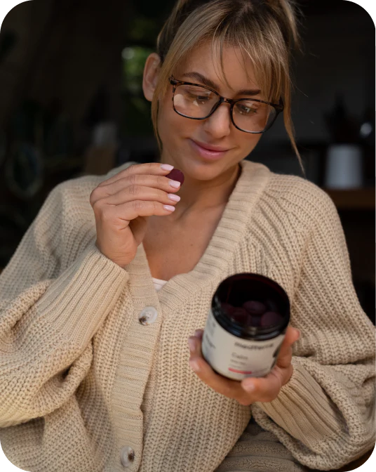 Woman holding a jar of CBD gummies and inspecting one gummy while seated in a cozy indoor setting