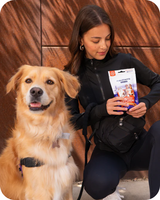 Woman kneeling with golden retriever, holding a medterra CHEWS dog supplement pouch