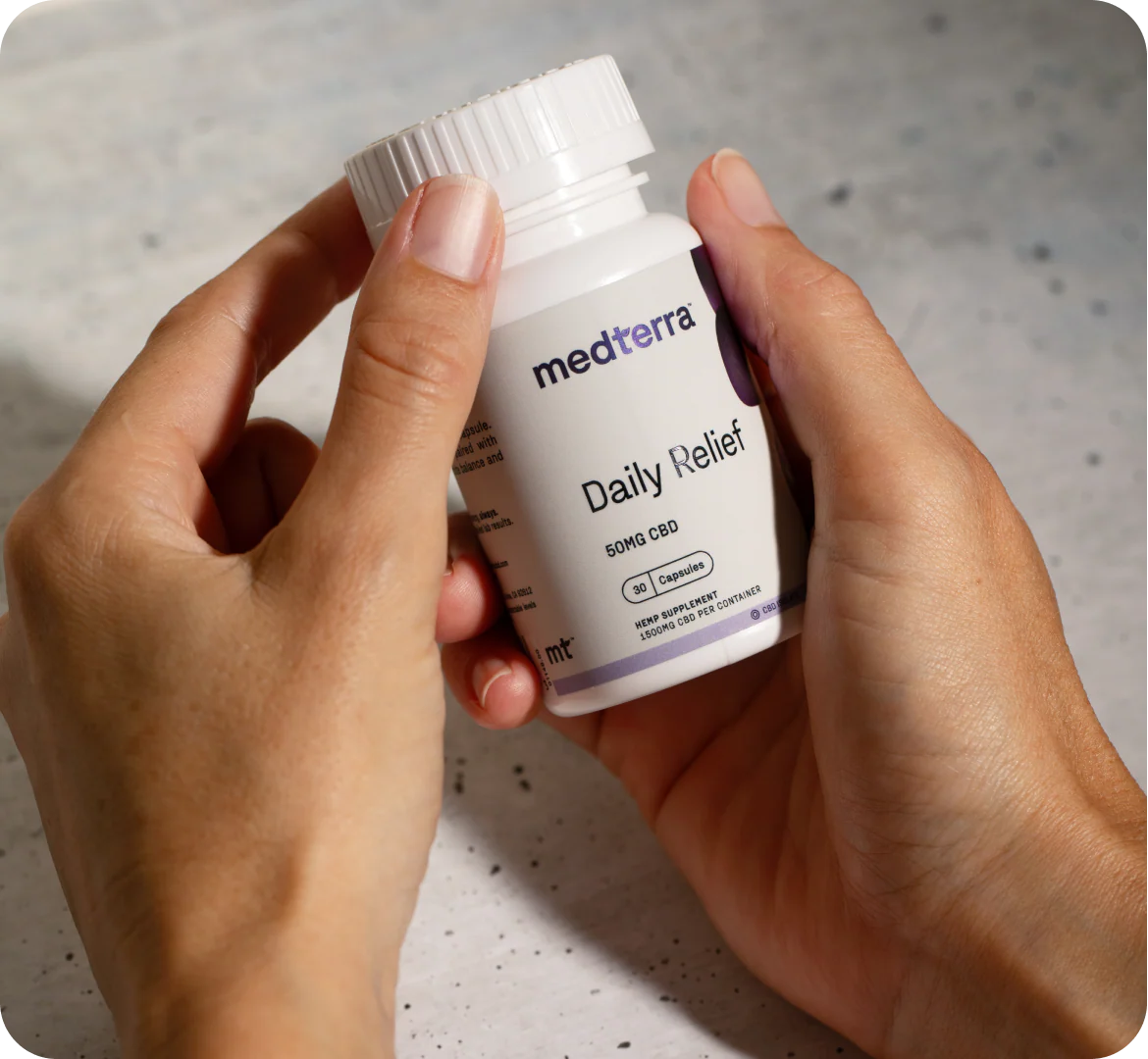 Angled close-up of Daily Relief CBD Isolate Capsules bottle held in hands, showing Medterra logo and “50MG CBD” text over a light stone surface