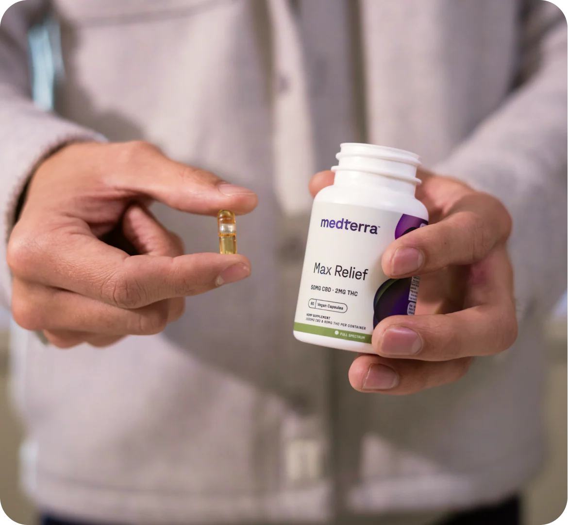 Close-up of Medterra Max Relief bottle showcasing a clear vegan softgel capsule held in hands against a neutral sweatshirt background