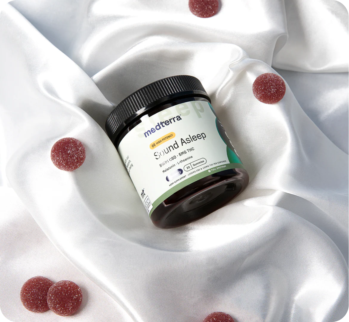 Angled jar of Sound Asleep THC gummies showing label Sound Asleep and 5 mg THC, red sugar-coated gummies on white satin fabric
