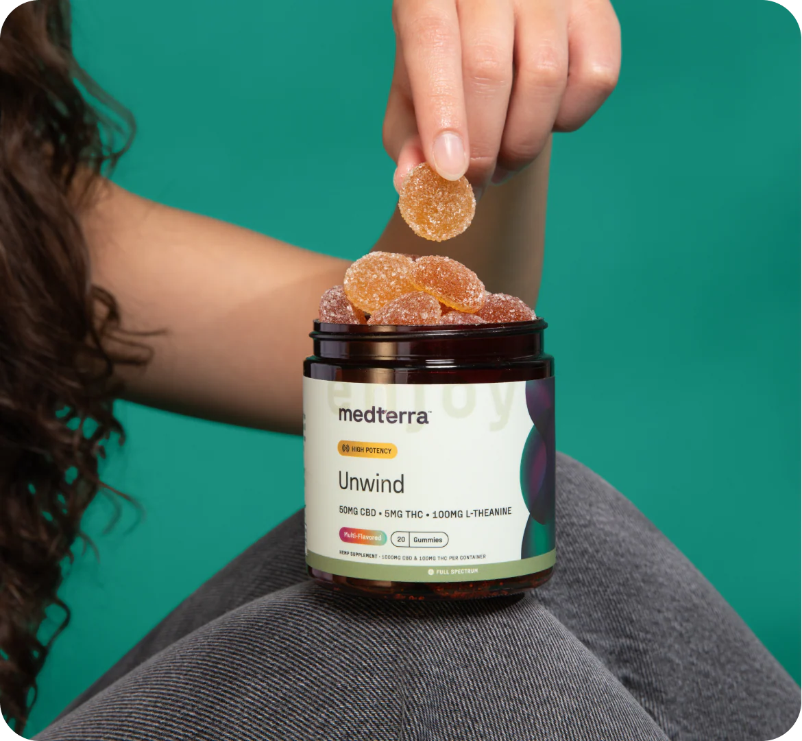 Close-up of Unwind Gummies jar with open lid and sugar-coated gummies, label reads 50 mg CBD, 5 mg THC, 100 mg L-Theanine on teal background