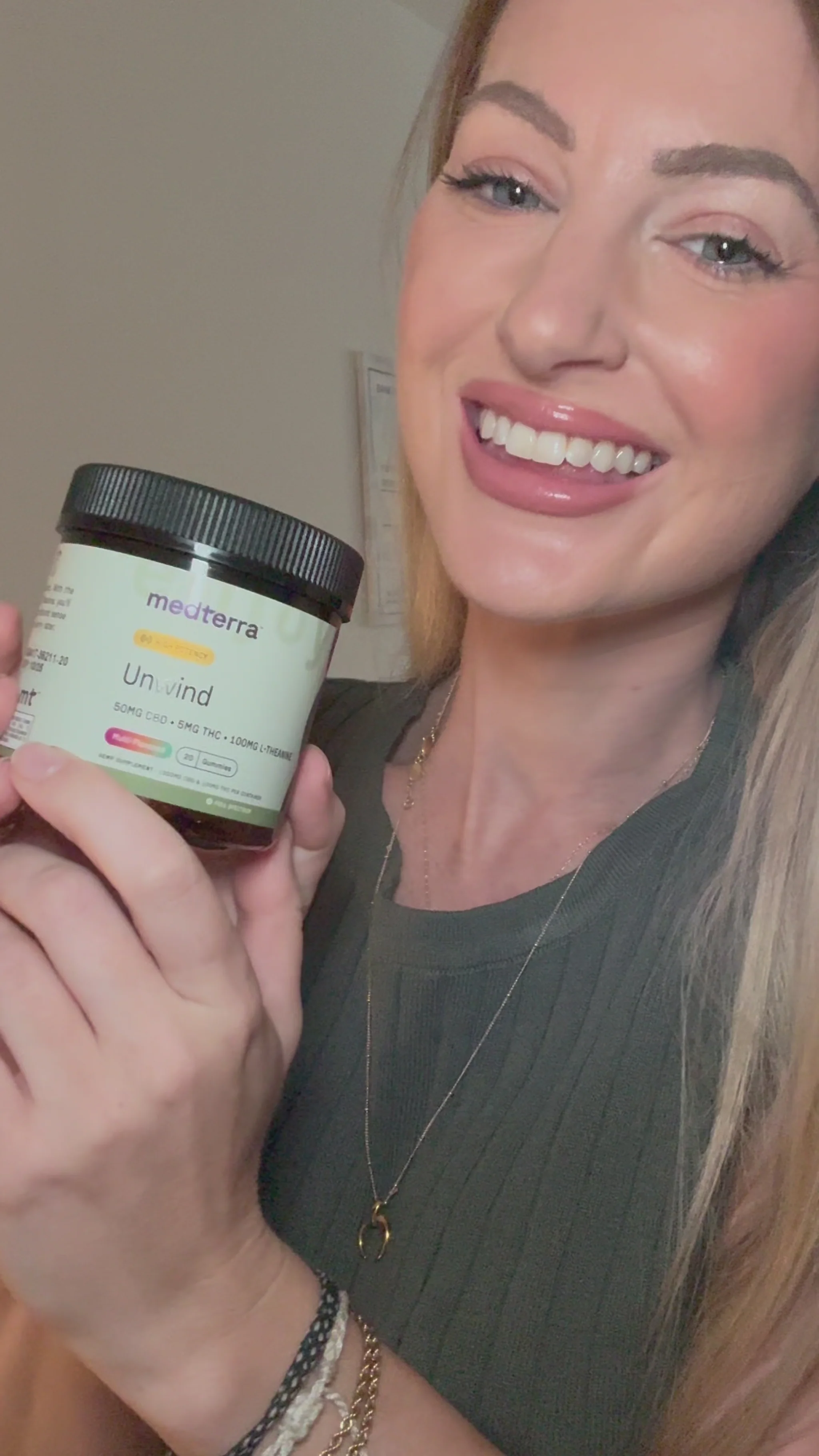Close-up of a smiling woman holding a jar of Medterra Unwind gummies showing label 50 mg CBD, 5 mg THC, 100 mg L-Theanine