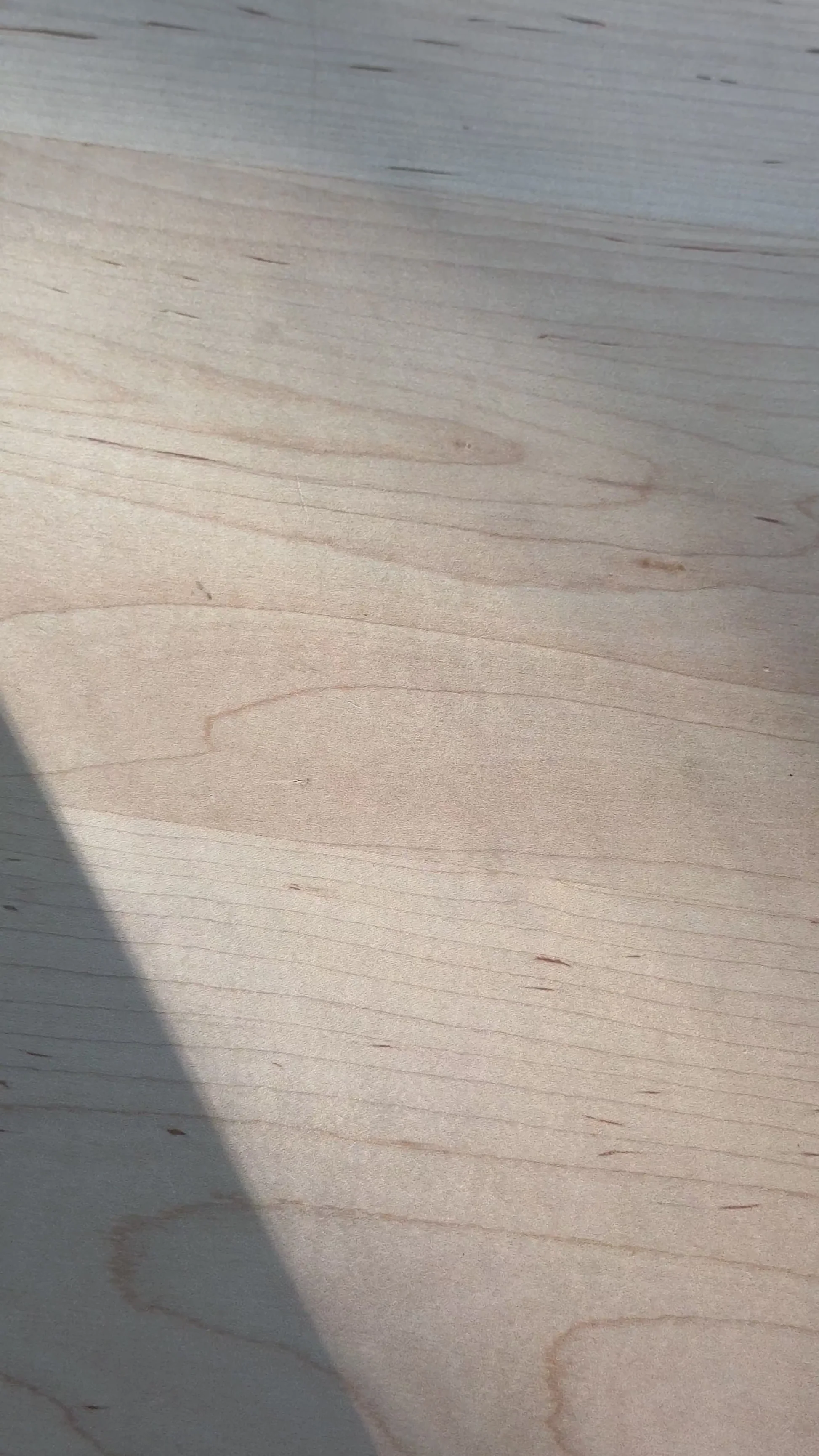 Light maple tabletop with diagonal shadow across the wood grain